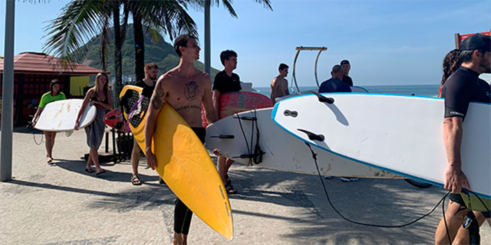 Grupo de pessoas com pranchas de surfe caminhando pela praia no Rio de Janeiro