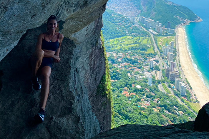 Mulher feliz encostada em paredão na trilha Garganta do Céu no Rio de Janeiro, com vista para a natureza ao redor.