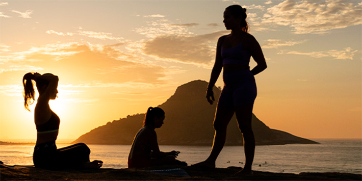 Três mulheres em praia do Rio de Janeiro com pôr do sol ao fundo
