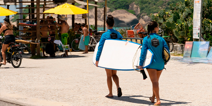 Grupo de amigos em praia no Rio de Janeiro segurando prancha de surf.